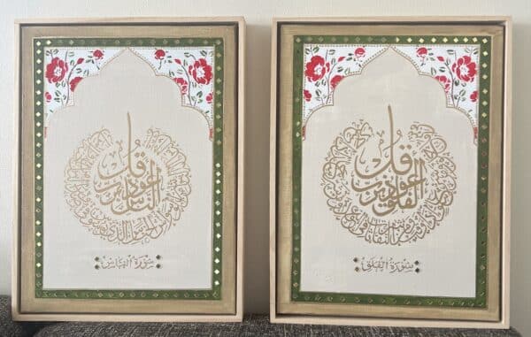 Surah Al Falaq & An Naas: Two framed Islamic calligraphy artworks in gold Arabic script, each with a floral border of red flowers and green leaves on a white background, set in ornate green and gold frames.