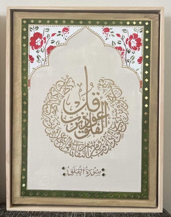 Surah Al Falaq & An Naas framed Islamic calligraphy art features gold Arabic script in a circular design on a cream background, bordered in green and gold, with a red-and-white floral pattern at the top.
